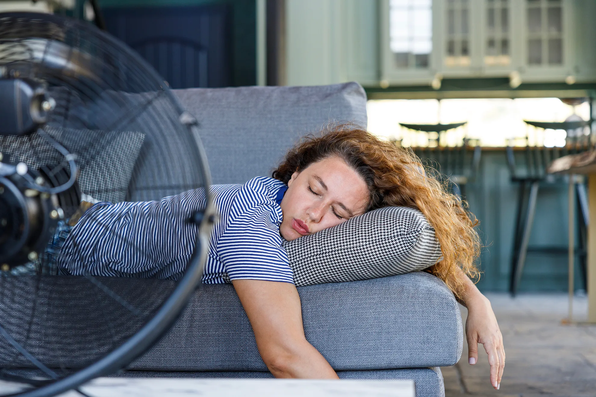 Femme endormie sur un canapé d'extérieur devant un ventilateur lors d'une nuit tropicale
